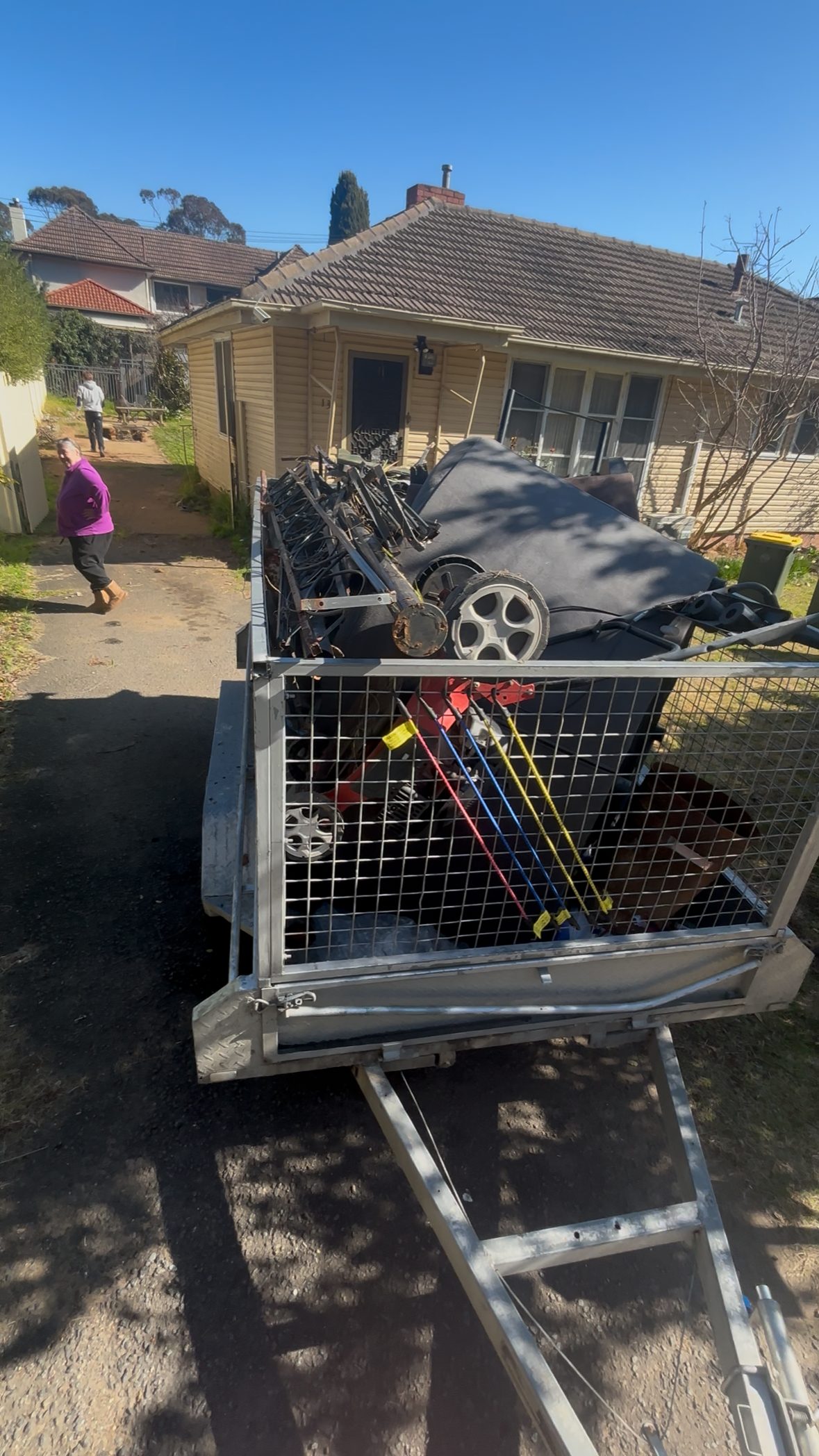 Loaded caged trailer in a Canberra driveway during a full property clean-out, with the client walking back to the house