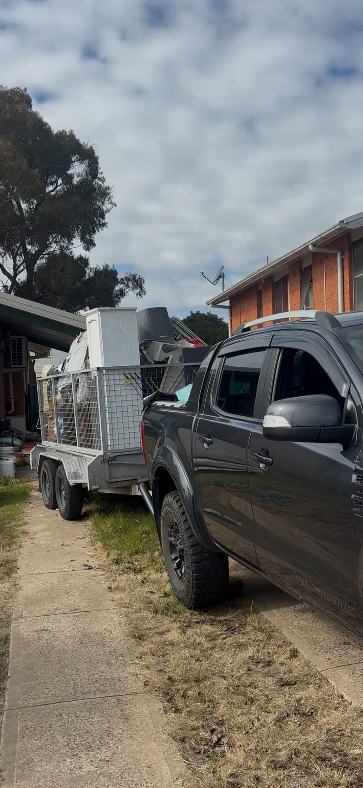 Sidekick ute and caged trailer loaded with household junk on a Canberra driveway